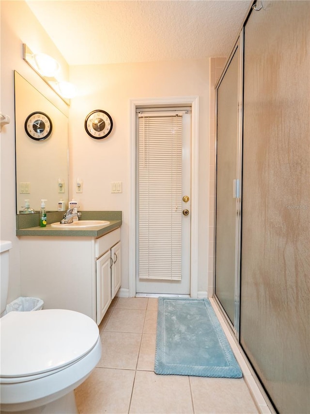 bathroom featuring a textured ceiling, toilet, vanity, tile patterned floors, and a stall shower