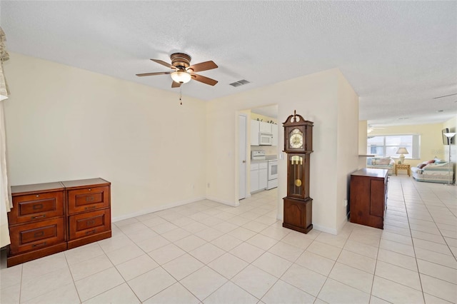 spare room with ceiling fan, light tile patterned floors, a textured ceiling, visible vents, and baseboards