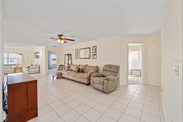 living area with light tile patterned floors, ceiling fan, baseboards, and a textured ceiling