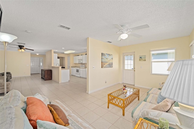 living room with a ceiling fan, visible vents, a textured ceiling, and light tile patterned floors