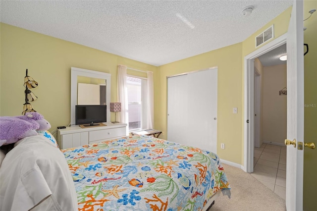 bedroom featuring a textured ceiling, light tile patterned floors, light carpet, visible vents, and a closet
