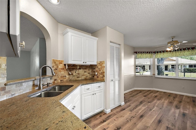 kitchen with white cabinets, wood finished floors, a sink, light stone countertops, and backsplash