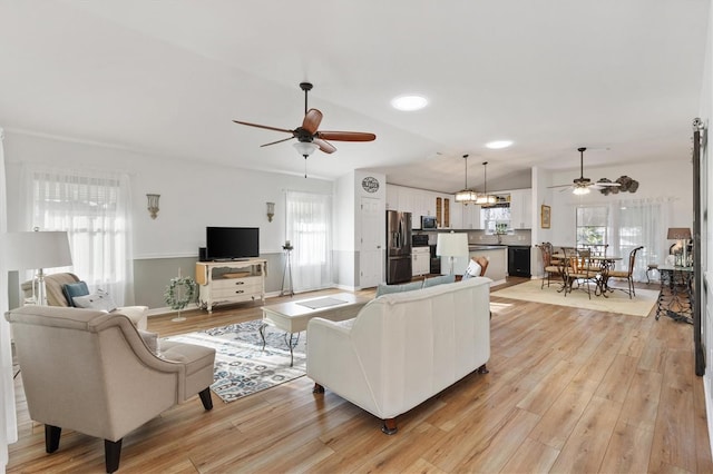 living room with lofted ceiling, a healthy amount of sunlight, light wood finished floors, and ceiling fan with notable chandelier