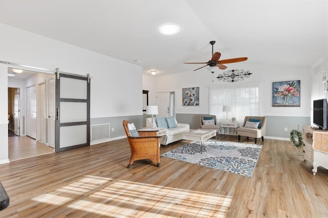 living room featuring lofted ceiling, a barn door, visible vents, and wood finished floors