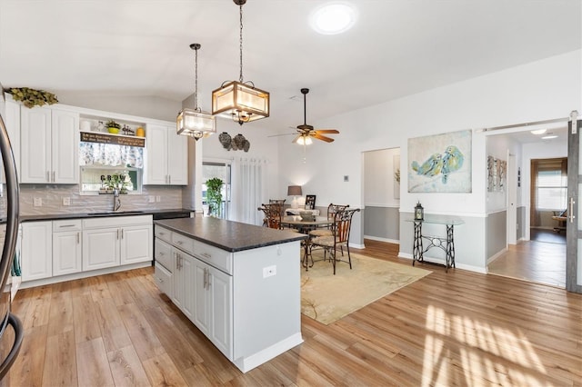 kitchen featuring a center island, dark countertops, light wood-style floors, white cabinetry, and a sink