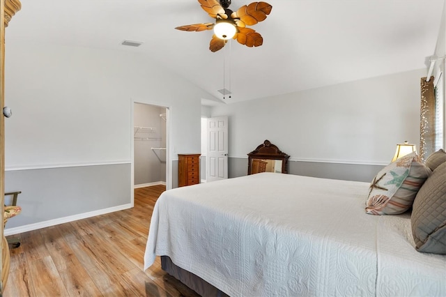 bedroom featuring wood finished floors, visible vents, baseboards, vaulted ceiling, and a walk in closet