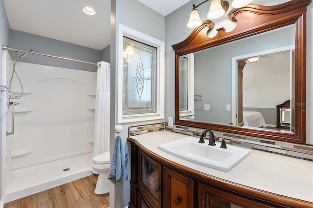 bathroom with toilet, a shower with shower curtain, wood finished floors, vanity, and tasteful backsplash