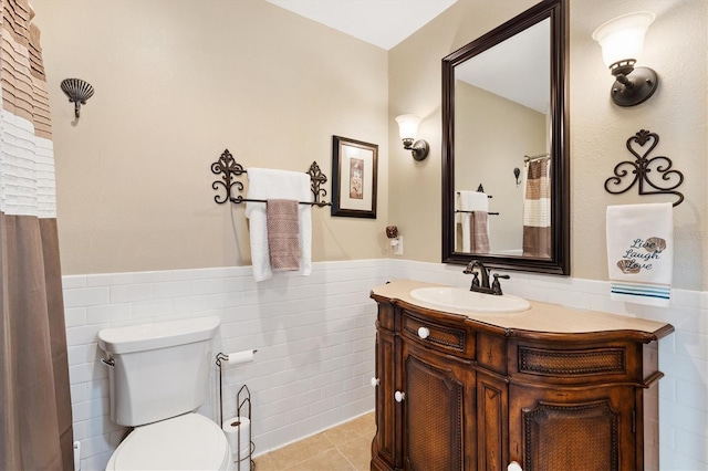 bathroom with tile patterned flooring, toilet, a wainscoted wall, vanity, and tile walls