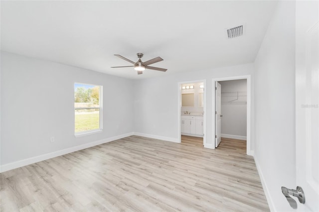 unfurnished bedroom featuring visible vents, light wood-style flooring, a spacious closet, ensuite bathroom, and baseboards