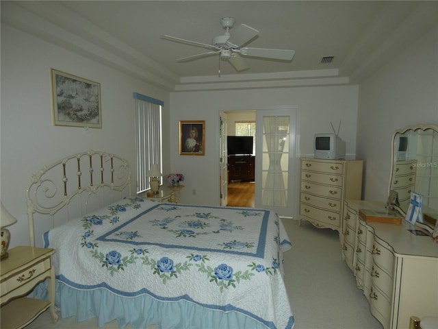 bedroom featuring ceiling fan, visible vents, a tray ceiling, and light colored carpet