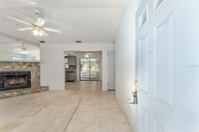 unfurnished living room with ceiling fan, baseboards, and a stone fireplace