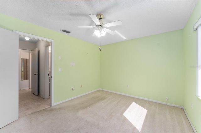 unfurnished room with a textured ceiling, light carpet, visible vents, baseboards, and a ceiling fan