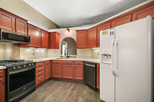 kitchen with arched walkways, dark wood finished floors, stainless steel appliances, light countertops, and a sink