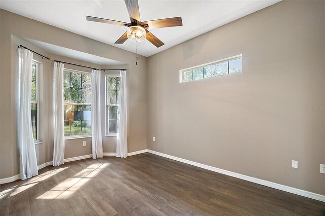 unfurnished room featuring a ceiling fan, baseboards, dark wood finished floors, and a wealth of natural light