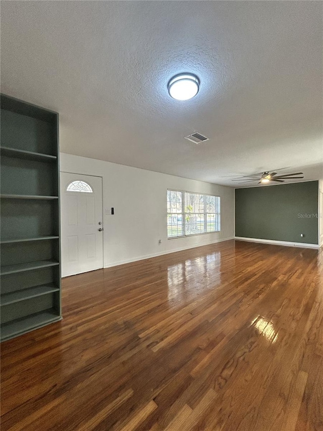 unfurnished living room featuring a textured ceiling, wood finished floors, visible vents, baseboards, and a ceiling fan