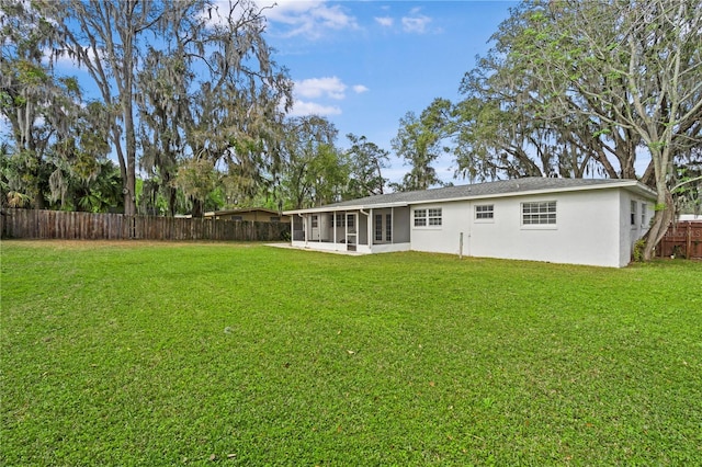 rear view of house featuring a lawn, fence, a sunroom, and stucco siding
