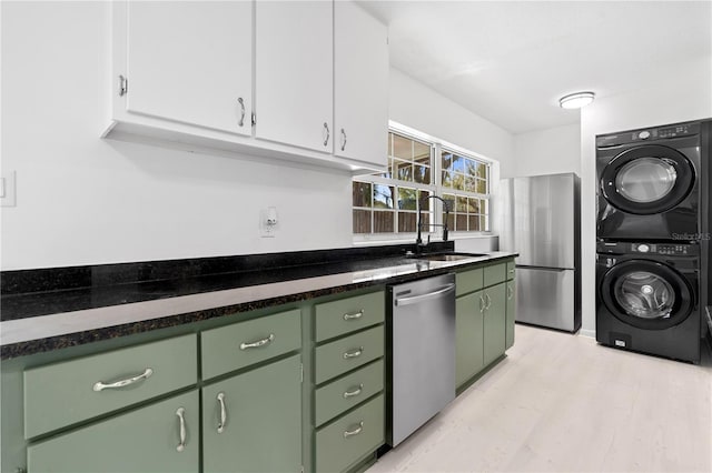 kitchen with stacked washer and clothes dryer, a sink, appliances with stainless steel finishes, green cabinets, and white cabinets