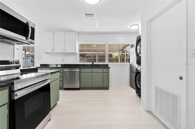kitchen featuring green cabinetry, stainless steel appliances, visible vents, and stacked washer / drying machine