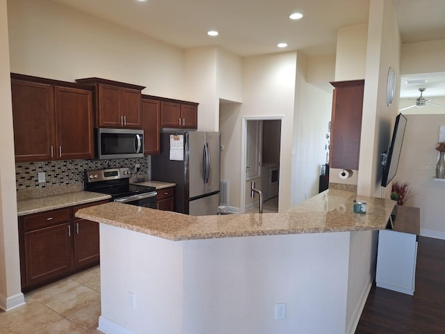 kitchen featuring recessed lighting, stainless steel appliances, a peninsula, backsplash, and light stone countertops