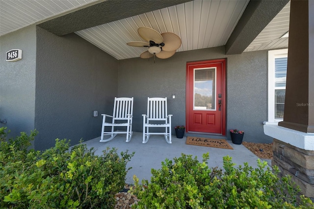 entrance to property featuring ceiling fan, a porch, and stucco siding