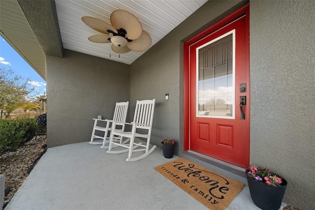 view of exterior entry with ceiling fan, a porch, and stucco siding