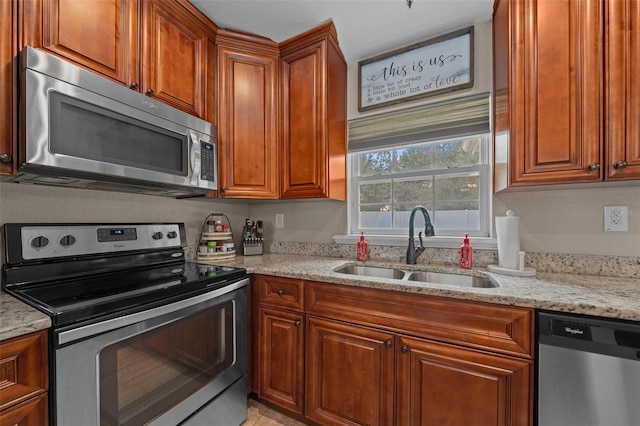 kitchen featuring stainless steel appliances, light stone counters, a sink, and brown cabinets