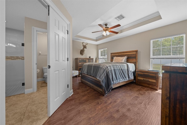 bedroom with wood finished floors, a raised ceiling, visible vents, and multiple windows