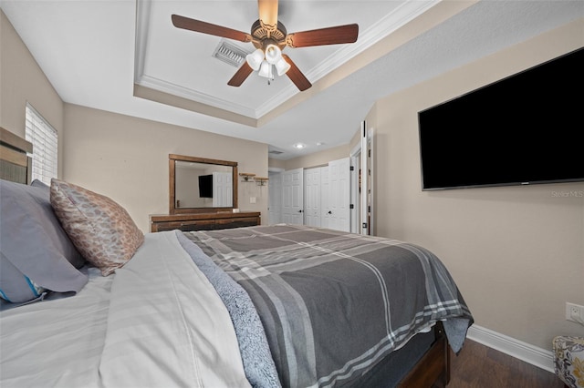 bedroom with baseboards, ornamental molding, wood finished floors, a tray ceiling, and a closet