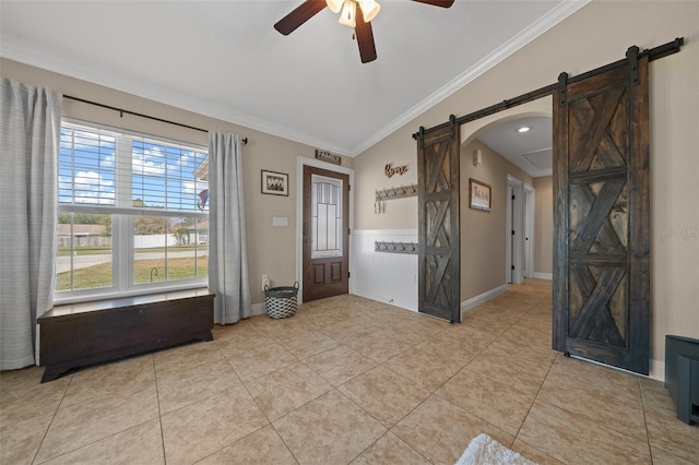 entryway featuring a barn door, ornamental molding, a ceiling fan, and light tile patterned flooring