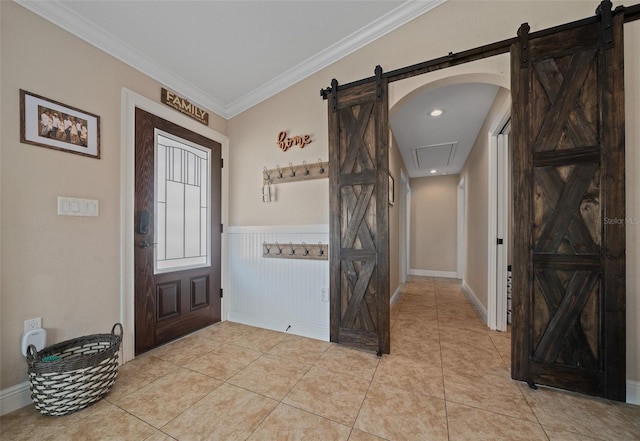 foyer with a wainscoted wall, a barn door, crown molding, and light tile patterned flooring