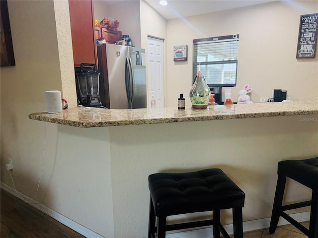 kitchen with a peninsula, baseboards, a breakfast bar area, and freestanding refrigerator