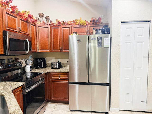 kitchen featuring stainless steel appliances, light stone countertops, brown cabinetry, and light tile patterned floors