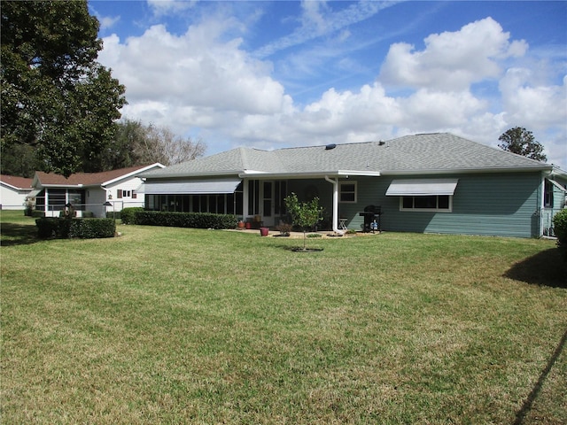 rear view of house with a yard, roof with shingles, and a sunroom