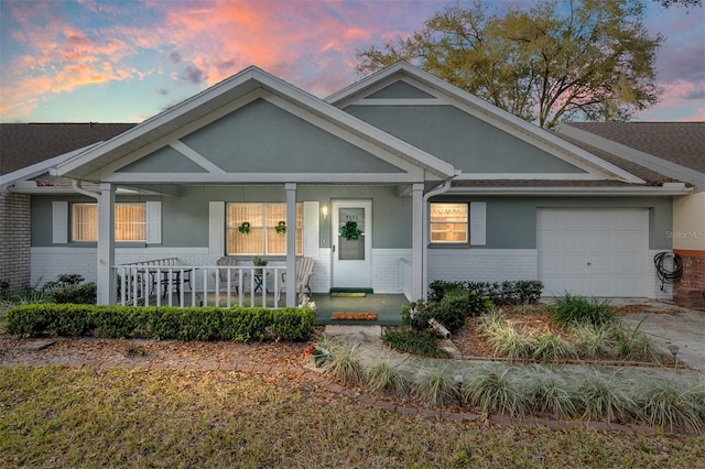 view of front of home featuring a garage, brick siding, a porch, and stucco siding