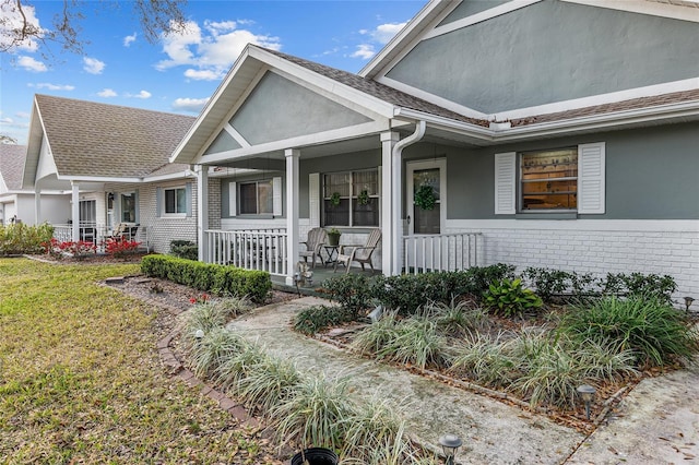 view of front of house featuring stucco siding, a front yard, a porch, and brick siding