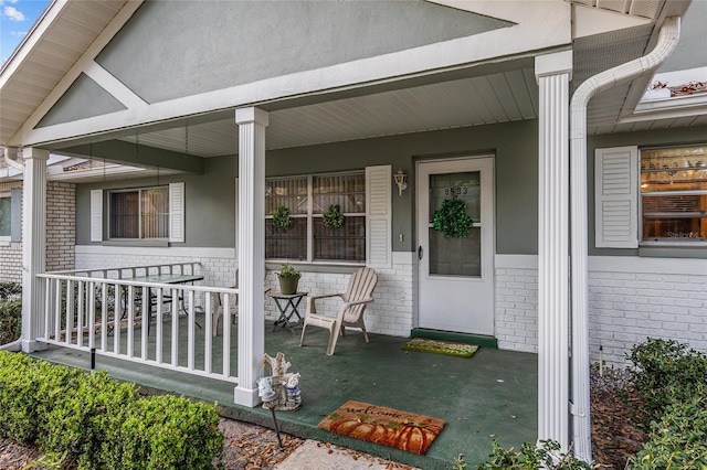 view of exterior entry with a porch and brick siding