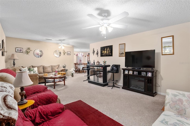 living room with baseboards, a ceiling fan, a glass covered fireplace, carpet, and a textured ceiling