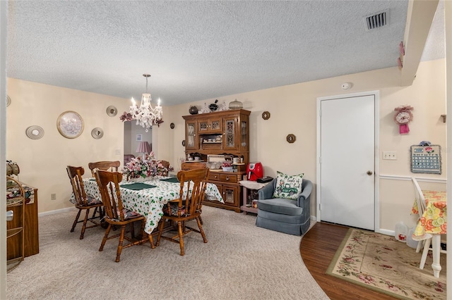 dining space with visible vents, light wood-style flooring, a textured ceiling, a chandelier, and baseboards
