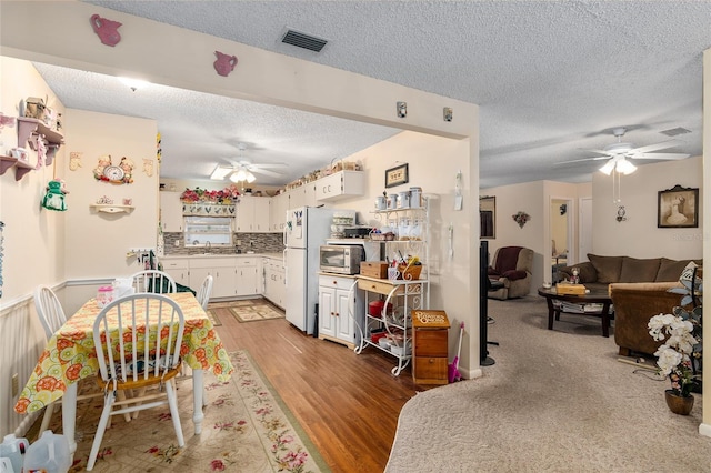 kitchen with visible vents, stainless steel microwave, light wood-style flooring, freestanding refrigerator, and white cabinetry