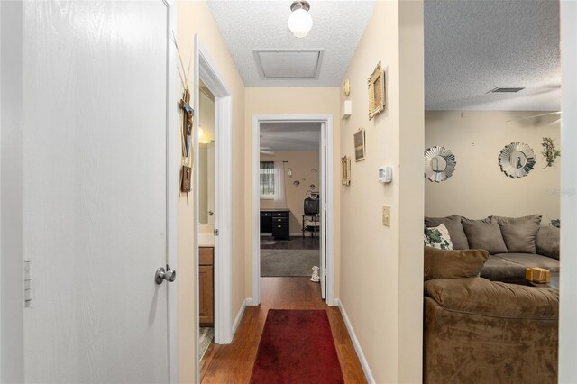 corridor with a textured ceiling, baseboards, and wood finished floors