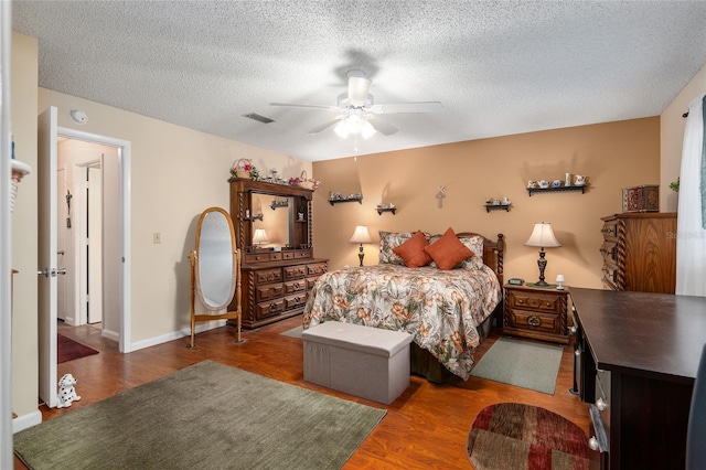 bedroom with a ceiling fan, visible vents, a textured ceiling, and wood finished floors