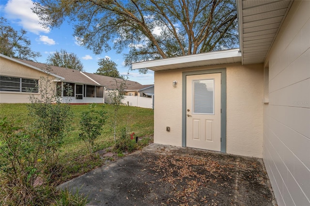 entrance to property with a yard, fence, and stucco siding