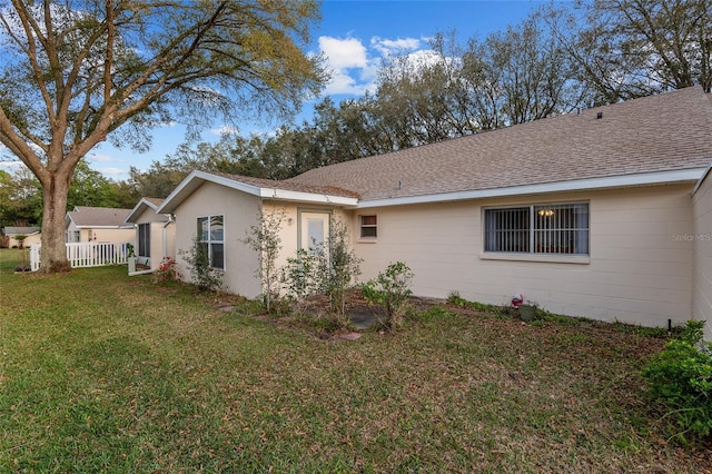 view of property exterior with roof with shingles, a lawn, and fence