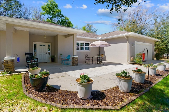 back of property featuring a garage, driveway, a patio, and stucco siding