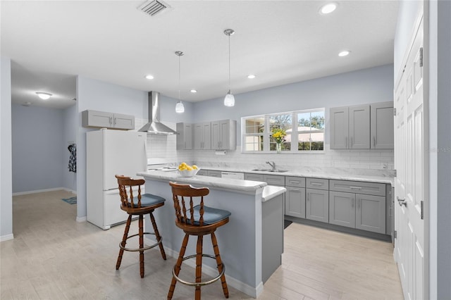 kitchen featuring wall chimney exhaust hood, gray cabinets, freestanding refrigerator, and a center island