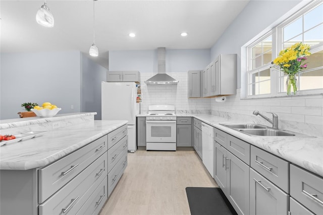 kitchen with gray cabinetry, white appliances, a sink, wall chimney range hood, and backsplash