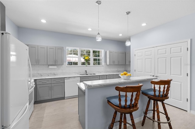 kitchen with white appliances, a breakfast bar area, gray cabinets, and tasteful backsplash