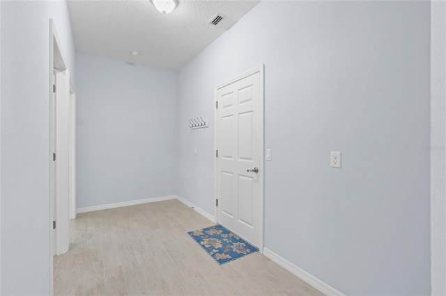 hall featuring a textured ceiling, wood finished floors, visible vents, and baseboards