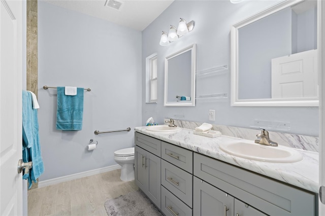 bathroom featuring wood finished floors, visible vents, a sink, and double vanity