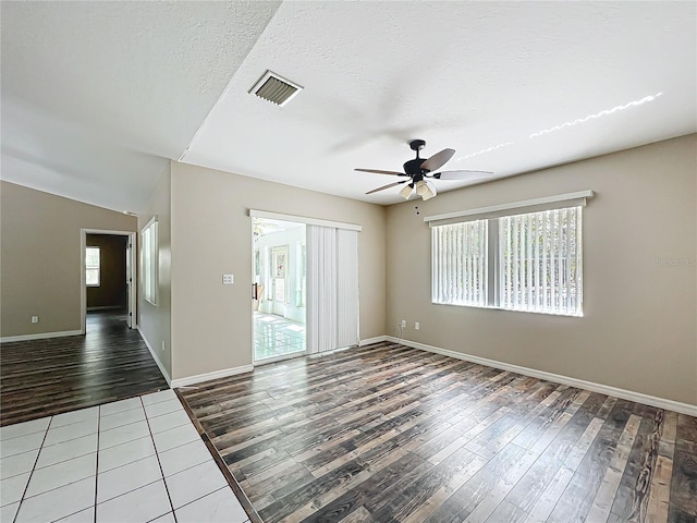 spare room featuring a textured ceiling, wood finished floors, a ceiling fan, visible vents, and baseboards